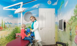 Kinderzahnärztin mit Kind im Behandlungszimmer für Kinder, mit bemalten Wänden, mit Märchenbildern