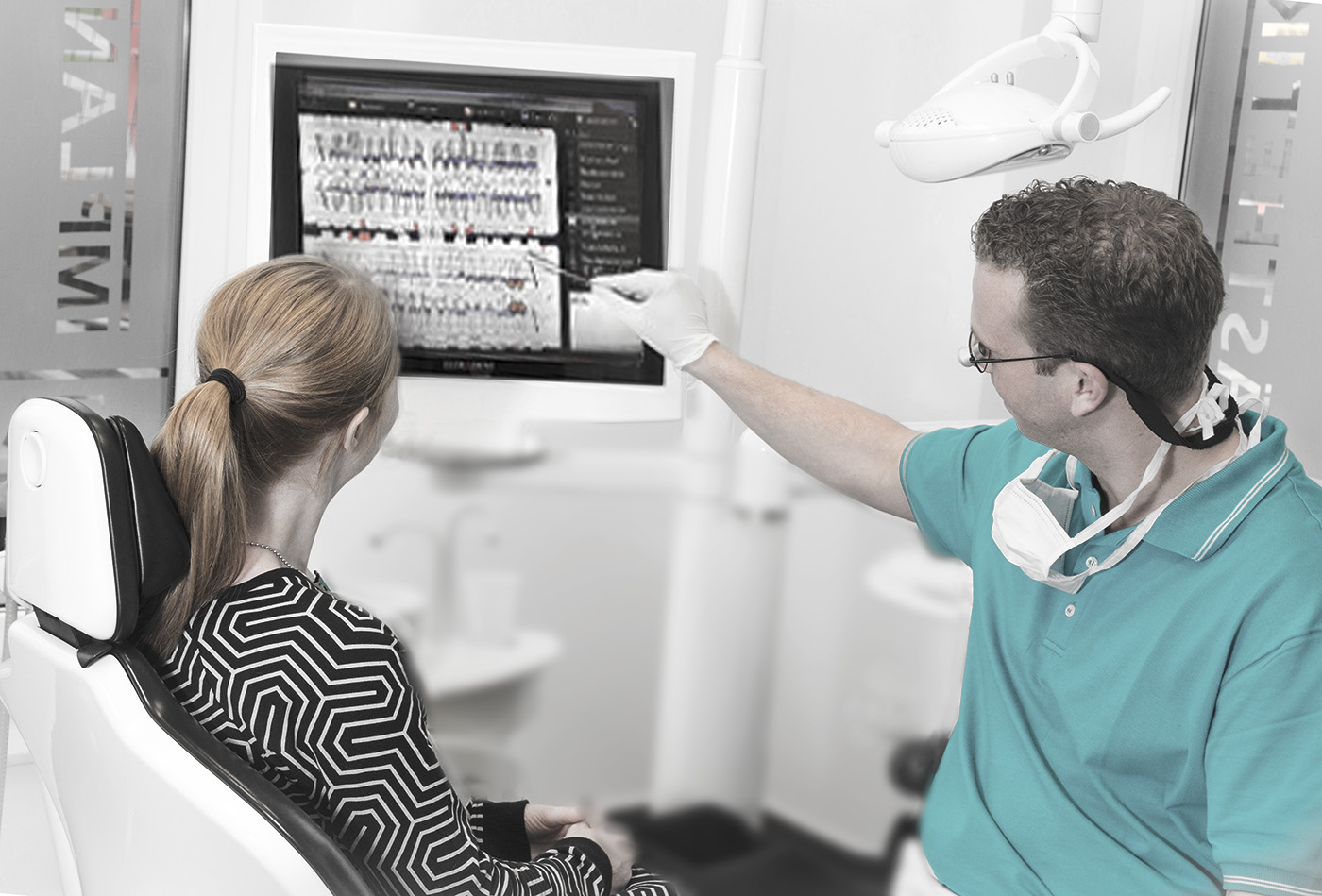 Zahnarzt bespricht mit einer Patientin den Zustand ihrer Zähne anhand einer Bilddarstellung am Computerbildschirm